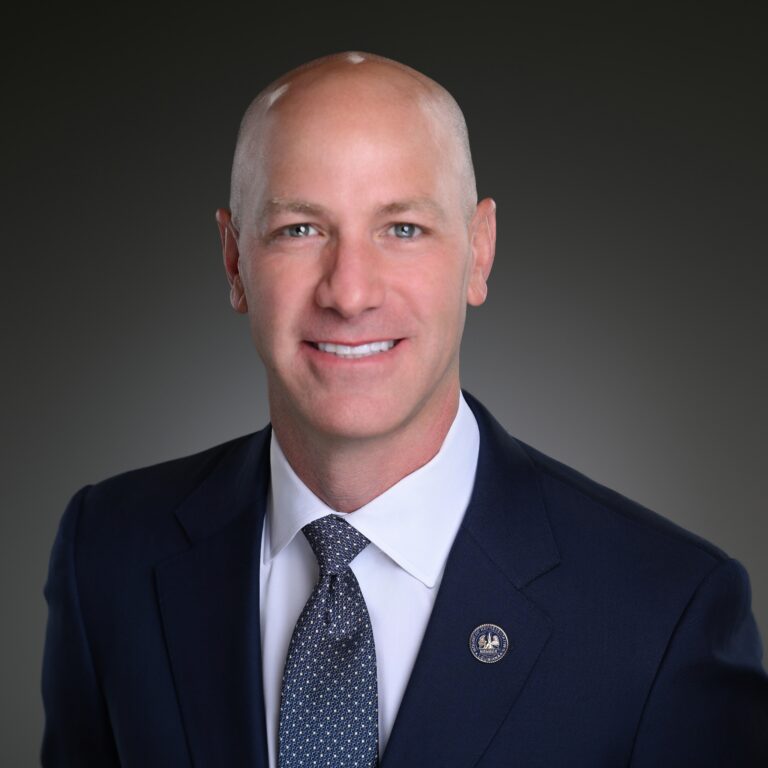 Headshot for Brach Myers wearing a navy suit and spotted white and navy tie with a white dress shirt.