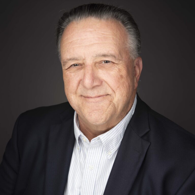 Headshot of Michael Bertaut wearing a dark blazer with a light white and blue striped dress shirt.