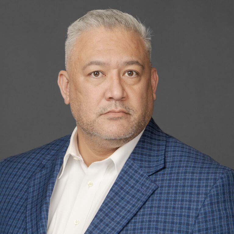 Headshot of Drew Contreras wearing a checkered navy blazer with a white dress shirt.
