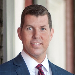 picture of James R. Raines wearing a navy suit and red tie with a white shirt.