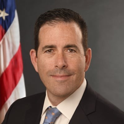 Bruce Greenstein wearing a dark suit with a blue tie and white shirt.